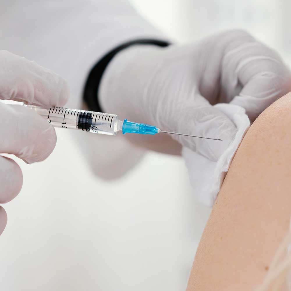 Therapeut spritzt eine Patientin am Oberarm